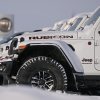 White Jeep Wranglers lined up in the snow at a dealership, a sign visible in the background.