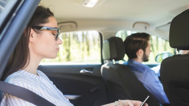 Woman texts on her phone while riding in a Lyft taxi car