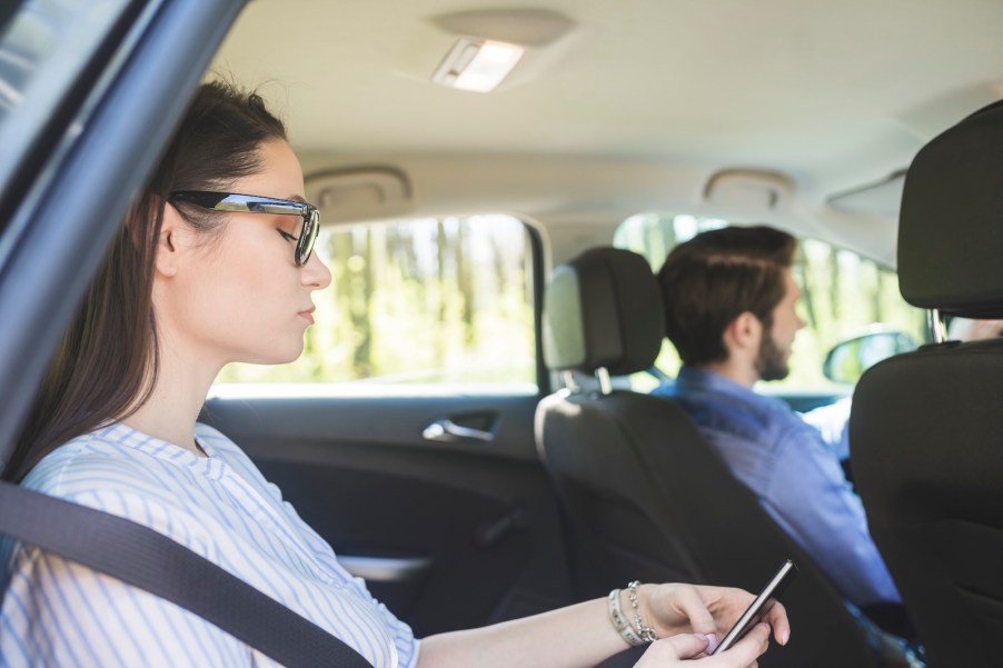 Woman texts on her phone while riding in a Lyft taxi car