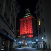 Red lights illuminate the Oakland City Hall, the buildings of a narrow alleyway visible in the foreground.