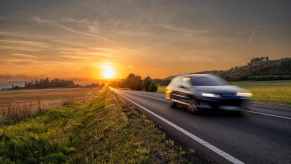 Sun sets behind a speeding car that's a blur on a rural highway.