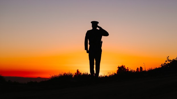 Silhouette of a military officer saluting in uniform, the sunset visible in the background.