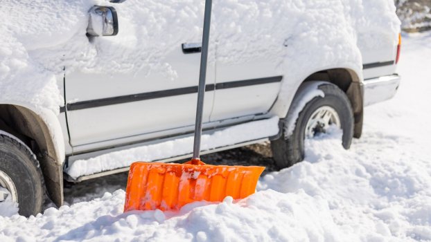 Orange shovel in front of white SUV covered in snow.