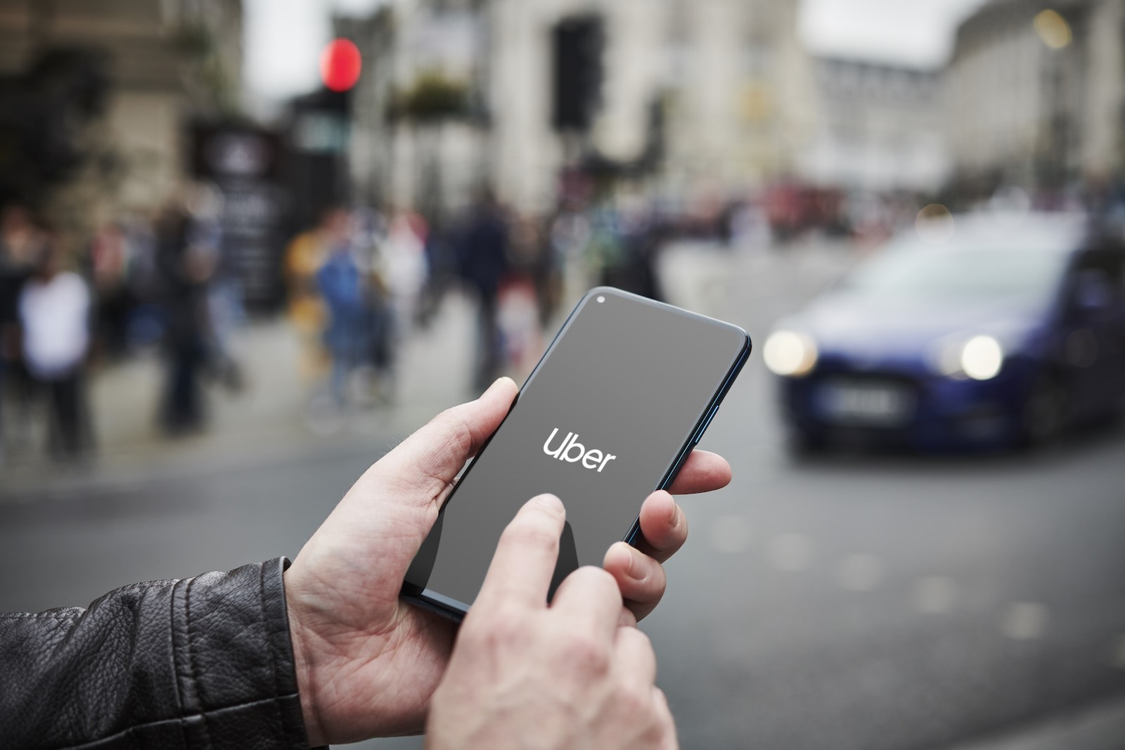 Man holding a smartphone starts the Uber app, a street full of cars visible in the background.