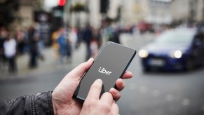 Man holding a smartphone starts the Uber app, a street full of cars visible in the background.