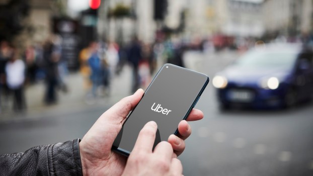 Man holding a smartphone starts the Uber app, a street full of cars visible in the background.