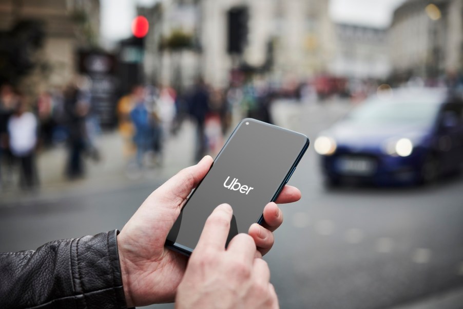 Man holding a smartphone starts the Uber app, a street full of cars visible in the background.
