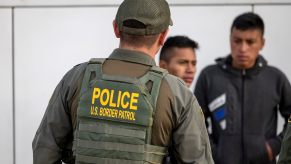 Border Patrol police officer in a green vest speaks with suspects during a traffic stop.