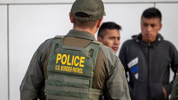 Border Patrol police officer in a green vest speaks with suspects during a traffic stop.
