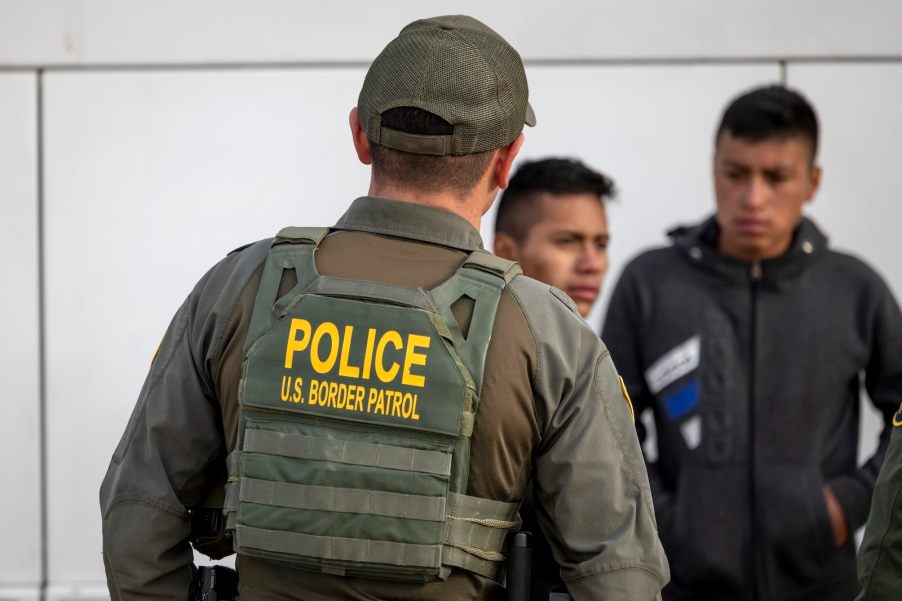 Border Patrol police officer in a green vest speaks with suspects during a traffic stop.