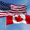 National flags of U.S. and Canada flying next to one another, blue sky in the background.
