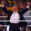 WWE CEO Vince Mcmahon stands in the ring with both his fists over his head.