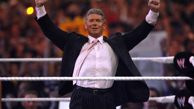 WWE CEO Vince Mcmahon stands in the ring with both his fists over his head.