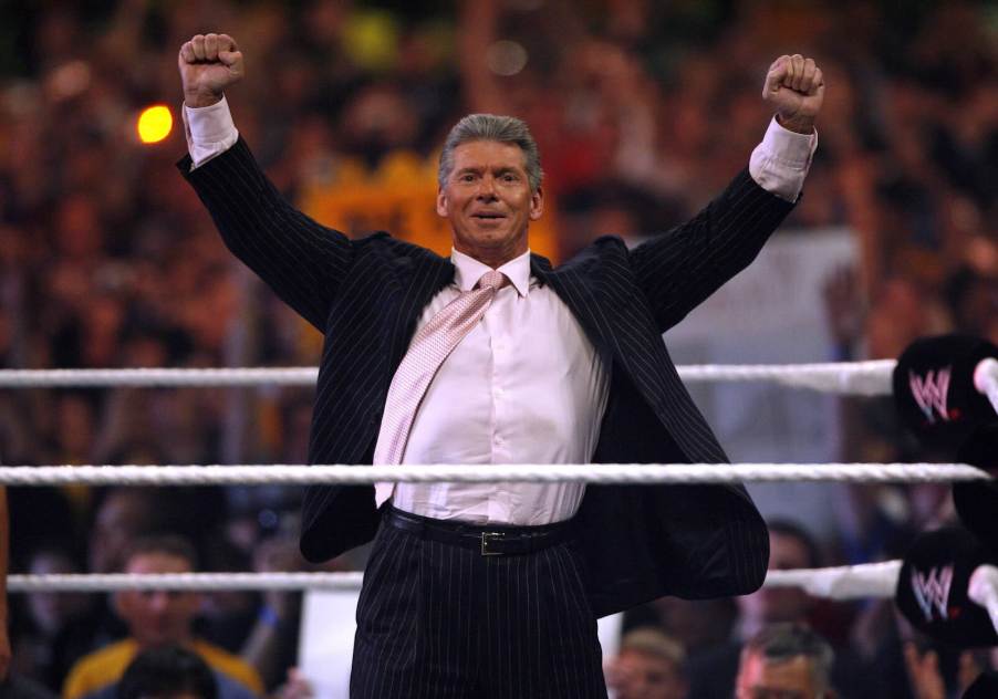 WWE CEO Vince Mcmahon stands in the ring with both his fists over his head.