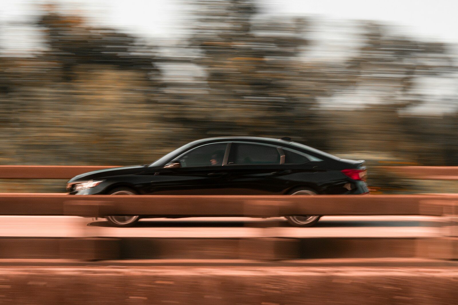 A black car driving on a bridge with trees in the background. Teen girls