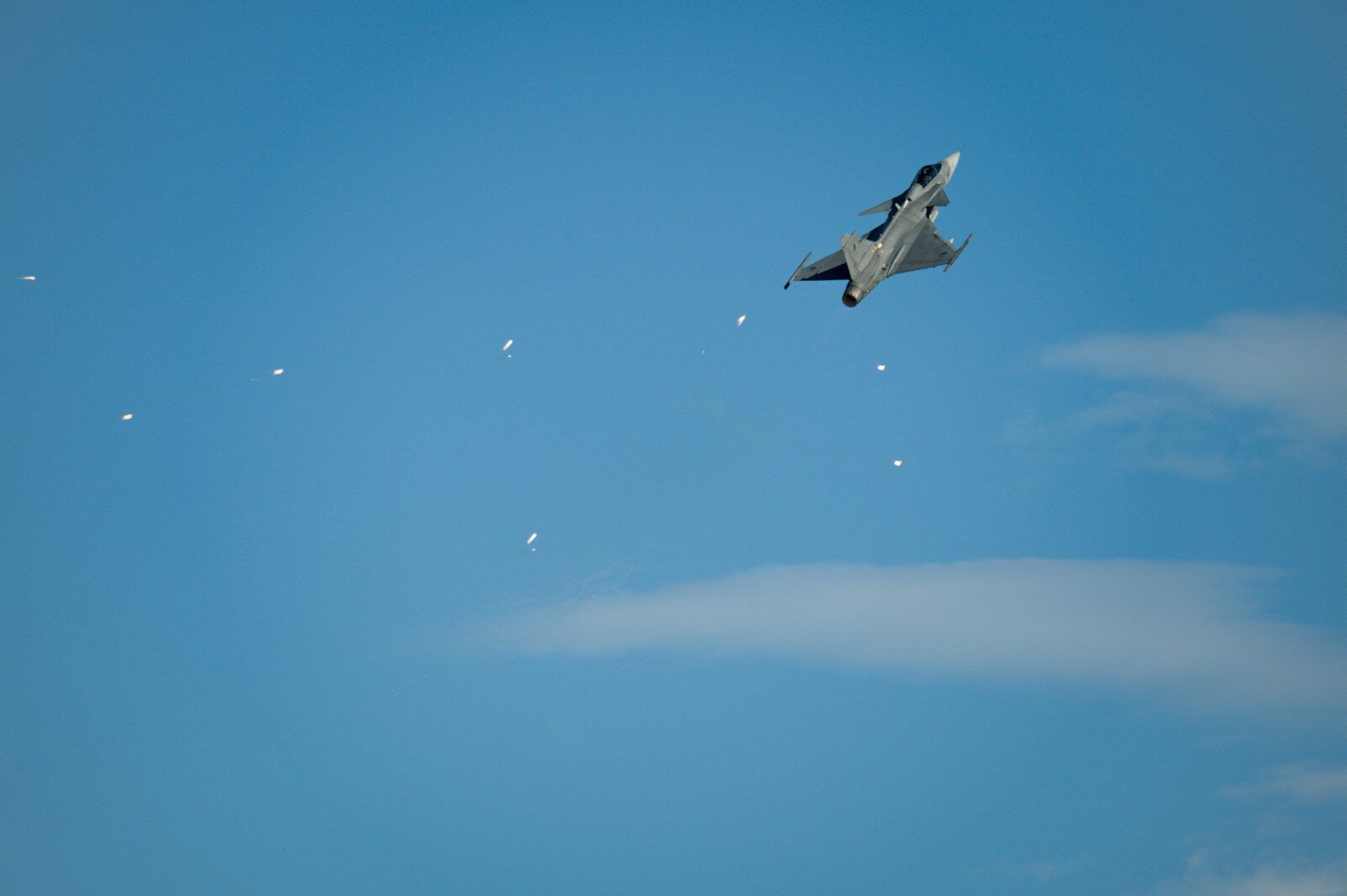 A fighter jet performs maneuvers against a clear blue sky aircraft