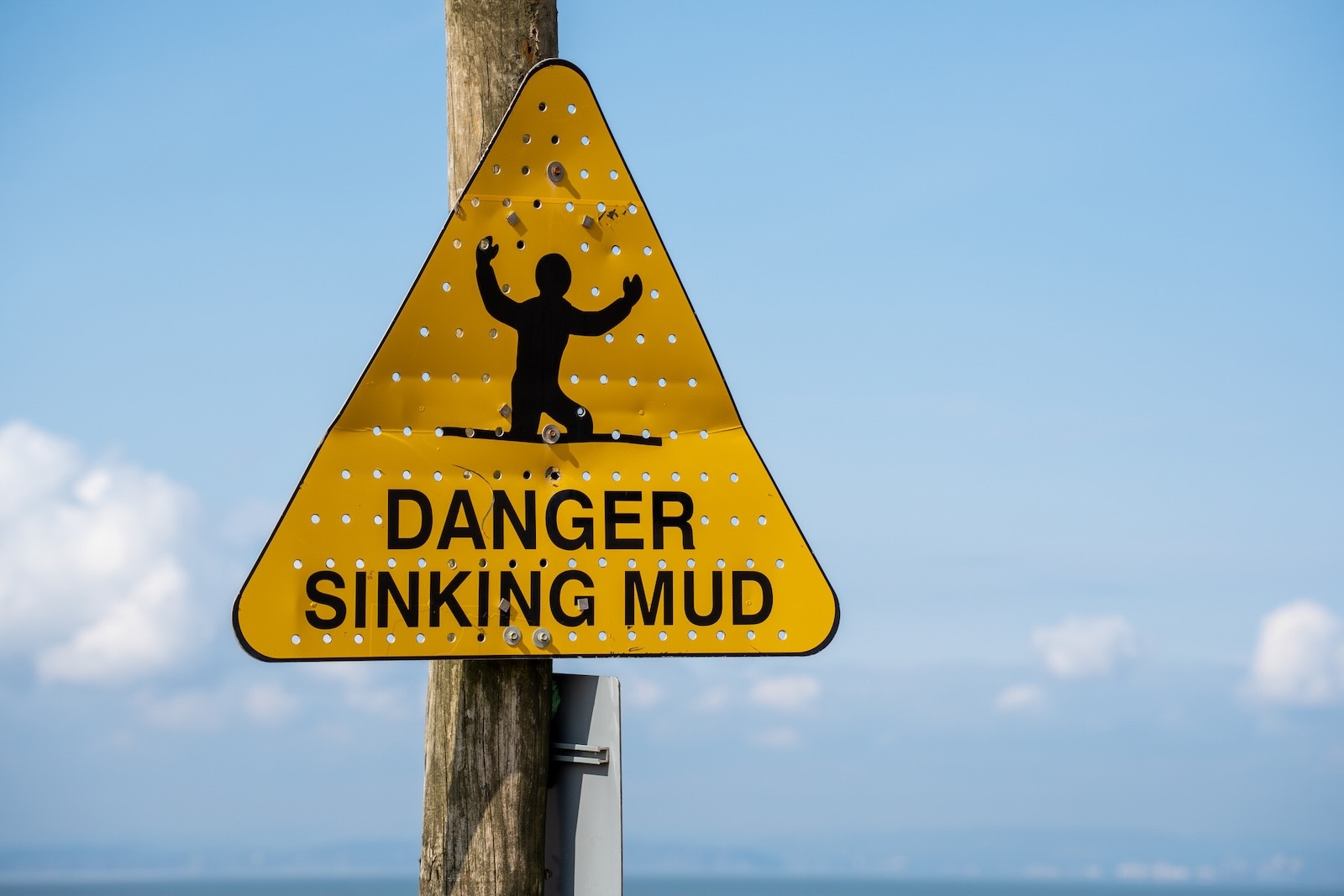 Yellow sinking mud warning sign in front of a blue sky,