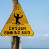 Yellow sinking mud warning sign in front of a blue sky,