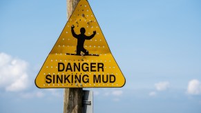 Yellow sinking mud warning sign in front of a blue sky,