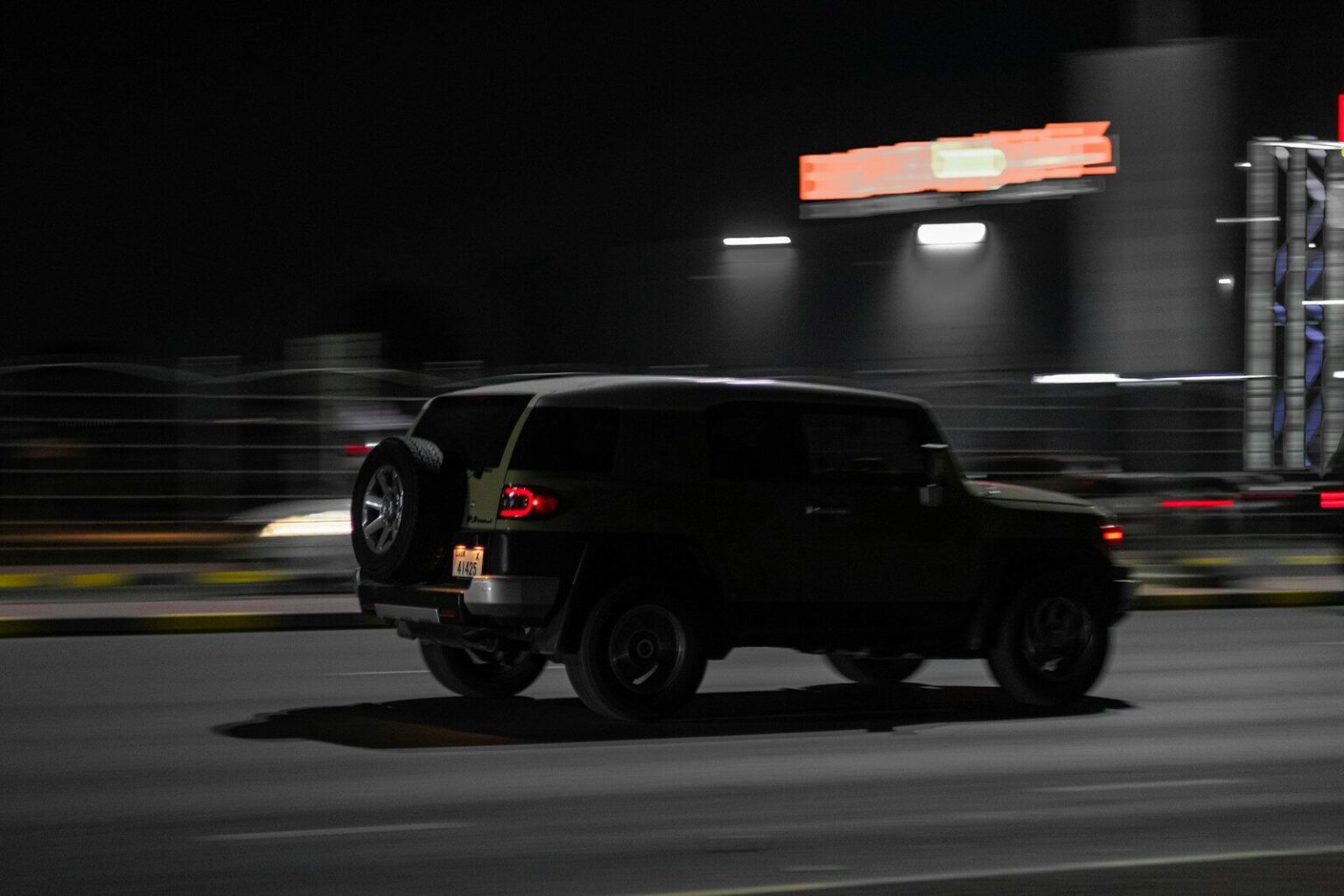 A dark car drives down a road at night.