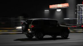 A dark car drives down a road at night.