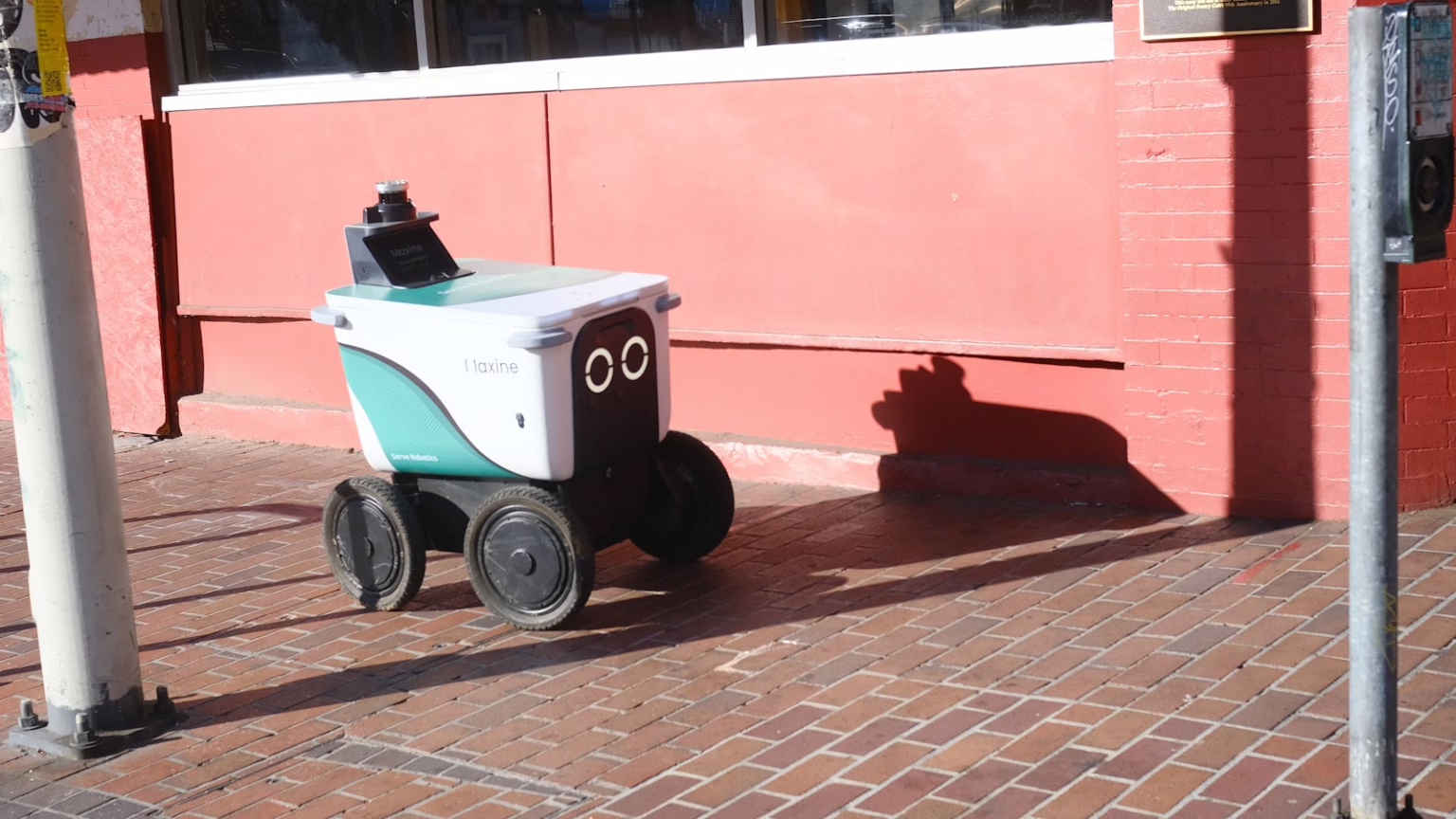 A small delivery robot with a face on the sidewalk.