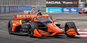 An orange race car speeds around a track. IndyCar