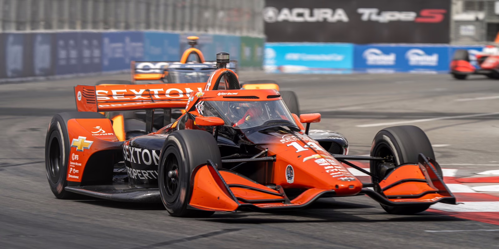 An orange race car speeds around a track. IndyCar
