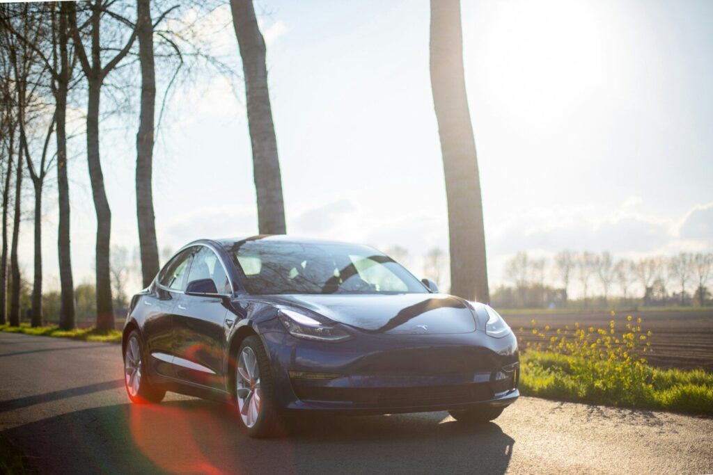 parked blue coupe beside trees during daytime. Tesla Model 3