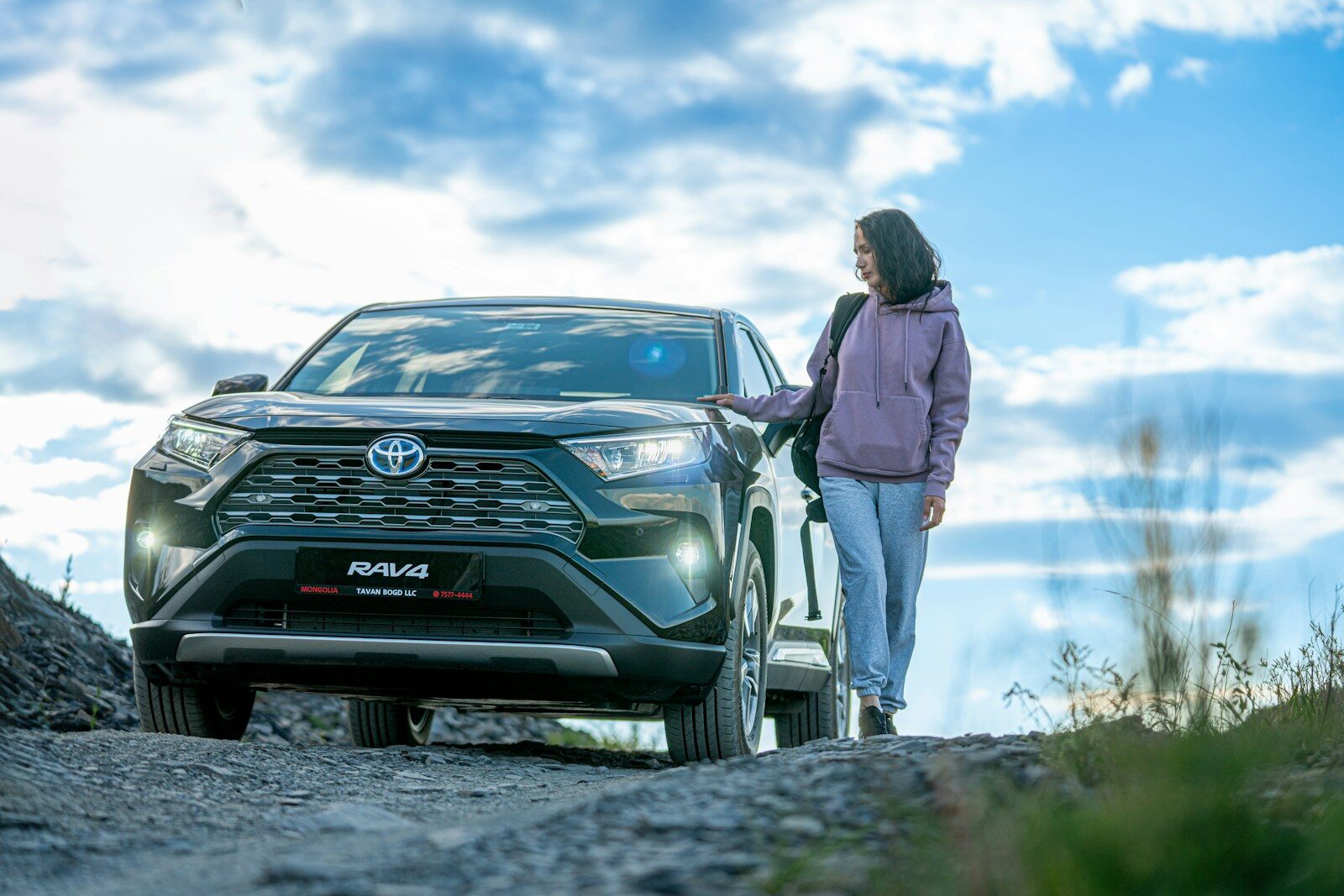 A woman standing next to a car on a dirt road