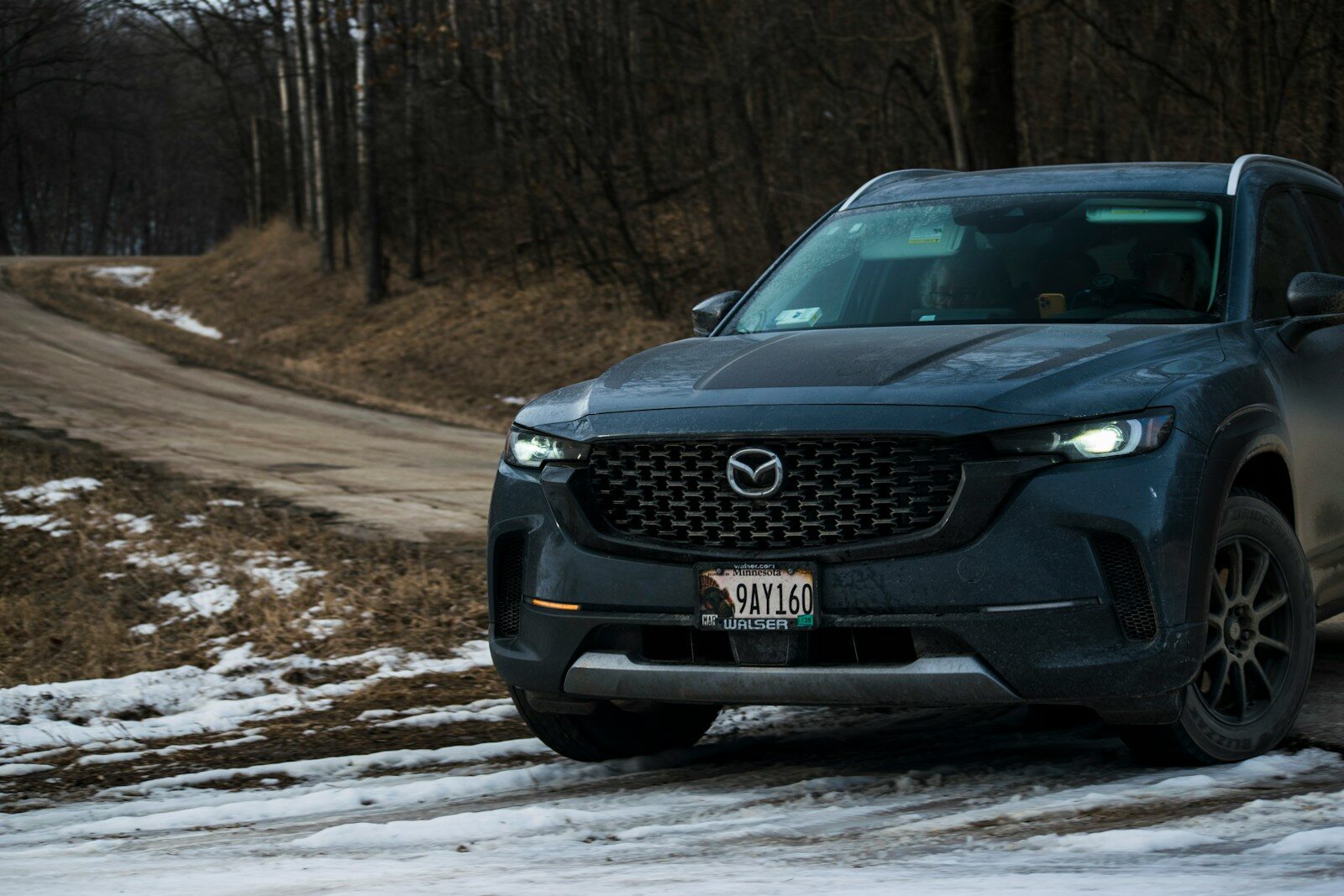 A blue suv parks on a snowy, dirt road.