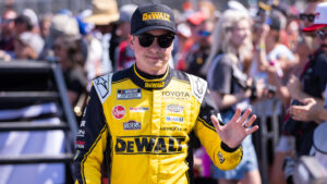 Christopher Bell waves to fans while wearing his yellow DeWalt Joe Gibbs Racing firesuit before a NASCAR Cup Series race.