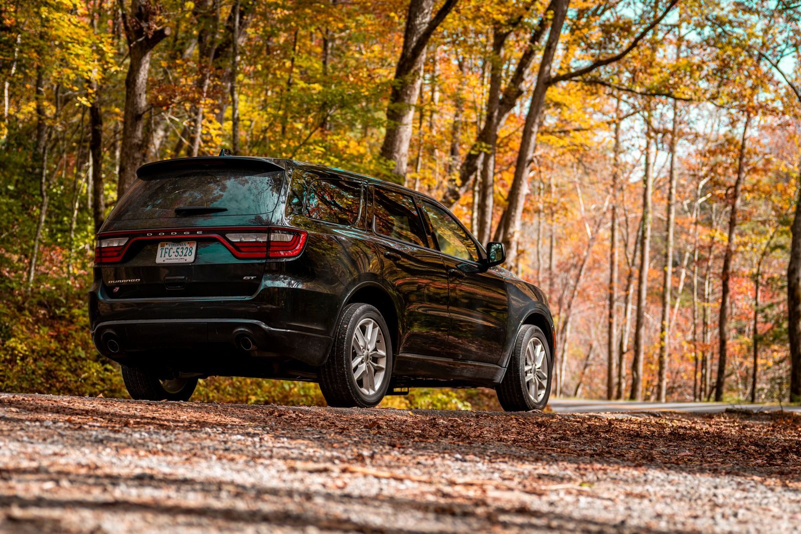 A sleek black SUV parked on a gravel road surrounded by autumn foliage, exuding a sense of adventure.