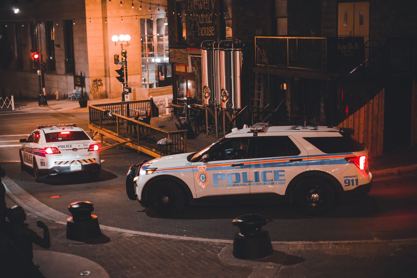 Two police cars patrolling a city street at night with warm lighting creating a dramatic urban mood.