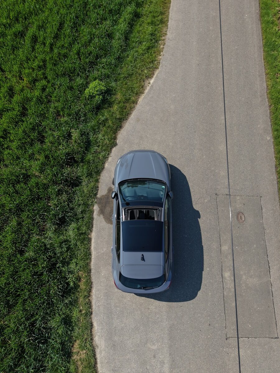 Gray car parked on an asphalt road with green grass