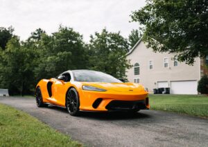 A sleek yellow supercar parked on a driveway against a suburban backdrop.