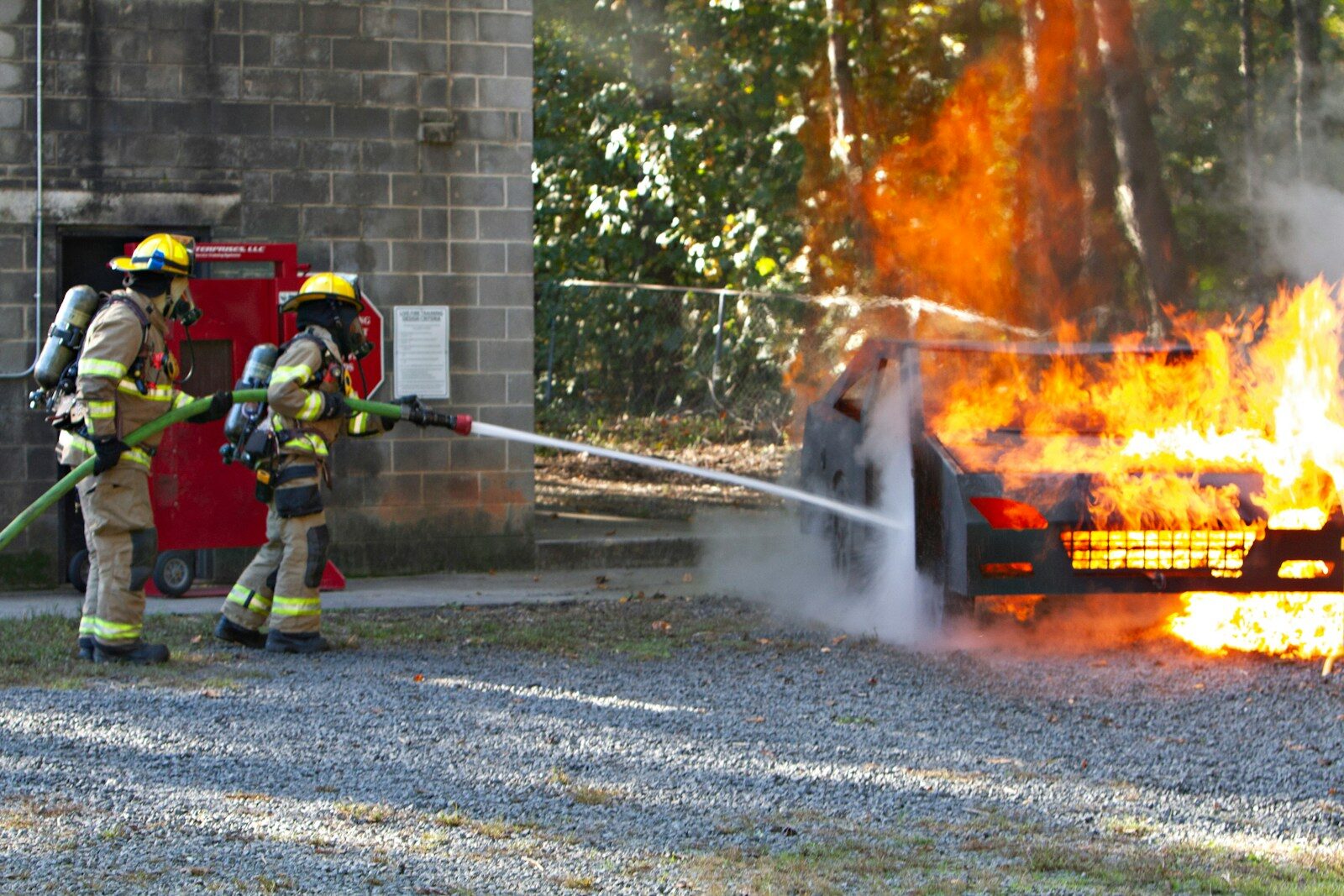 Two firemen fighting a car fire with a hose